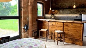 A rustic kitchen with a wooden bar, two stools, and a large window overlooking a green landscape. - Podere Montevalle's Clubhouse (Provincia di Piacenza)