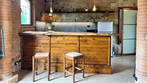 A rustic kitchen with a wooden island, two stools, hanging light fixtures, and a stone wall. - Podere Montevalle's Clubhouse (Provincia di Piacenza)