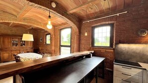 A rustic kitchen with a long wooden table, hanging light bulbs, and brick walls. - Podere Montevalle's Clubhouse (Provincia di Piacenza)