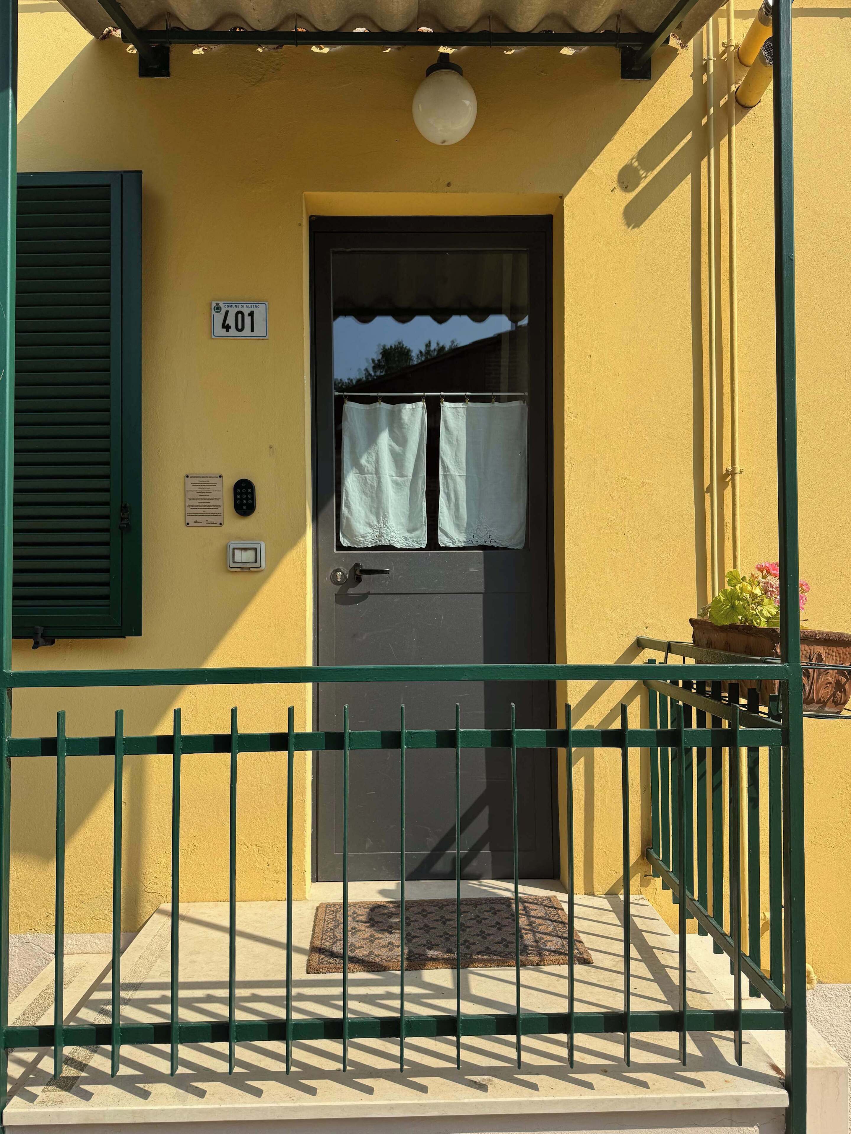 Un bâtiment jaune avec une porte noire, un portail vert et un panneau indiquant le numéro « 401 » au-dessus de la porte.