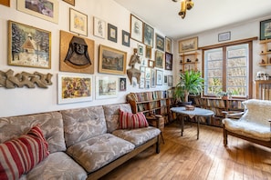 A cozy room with a sofa, a wooden table, a bookshelf, and various framed artworks on the walls.