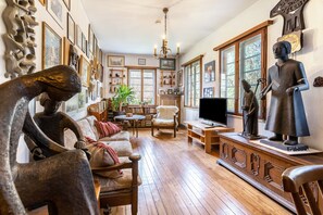 Una habitación con suelo de madera, un sofá, una silla, un televisor y varias esculturas y pinturas en las paredes.