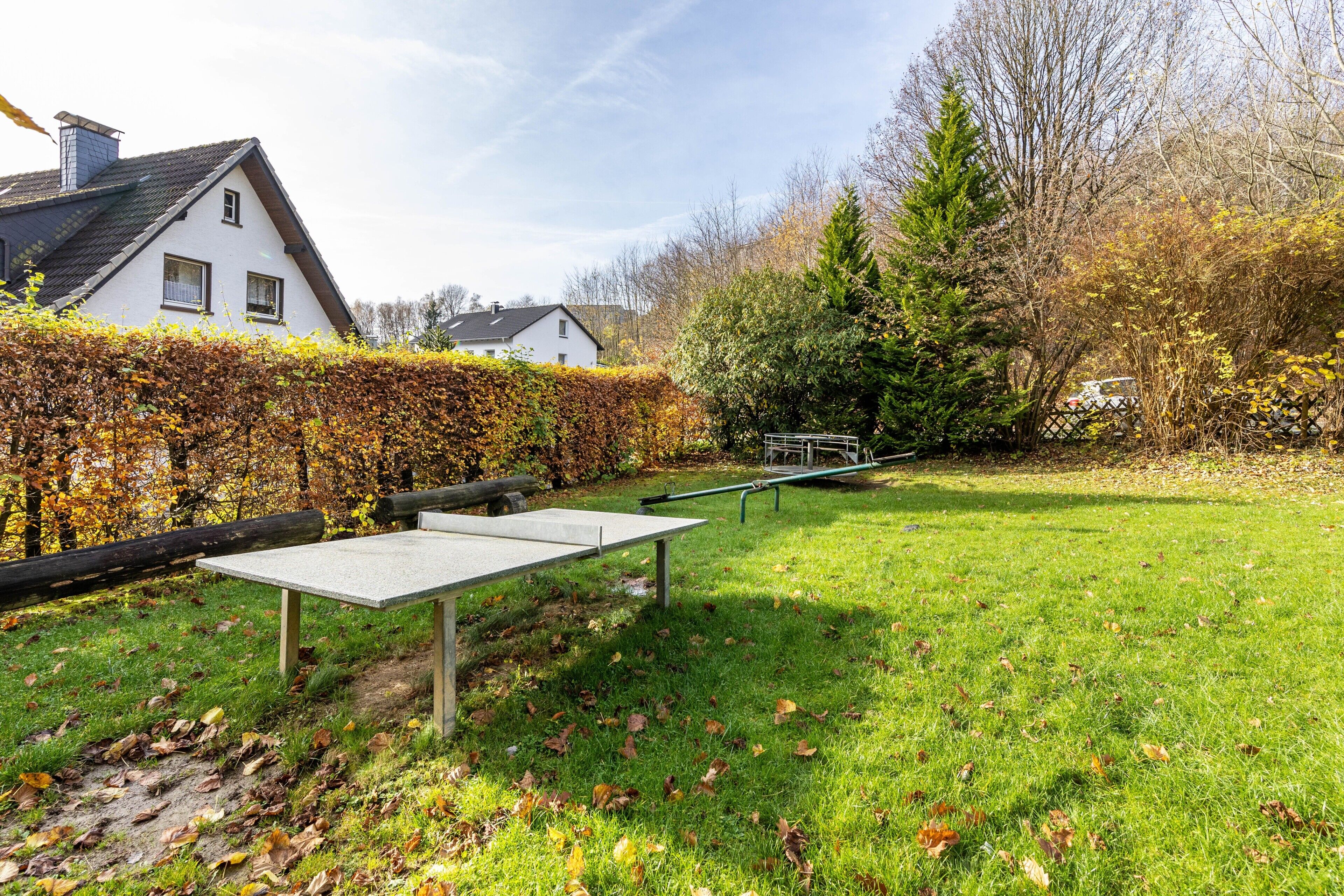 A grassy outdoor area with a bench, a wooden fence, and a hedge.