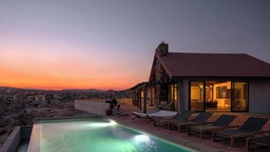 Une villa moderne dotée d’une piscine, d’un espace salon extérieur et offrant une vue sur le paysage désertique au coucher du soleil.