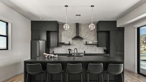 A modern kitchen with a central island, bar stools, and pendant lighting.