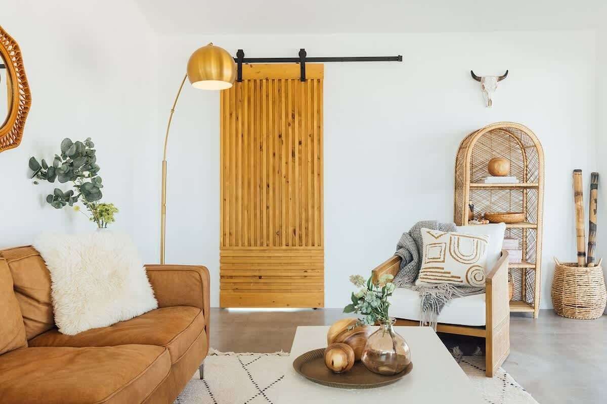 Ein modernes Wohnzimmer mit einer braunen Ledersofa, einer weißen, flauschigen Decke, einer Wand aus Holzlamellen, einer Hängeleuchte, einem gewebten Korb und einem dekorativen Wandbild.
