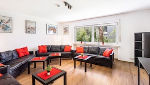 A modern living room with leather sofas, red cushions, wooden tables, and artwork on the walls. - Guesthouse with Shared Garden and Wi-Fi (Finnentrop)