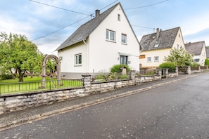 A residential street with houses, a stone wall, and a paved road.
