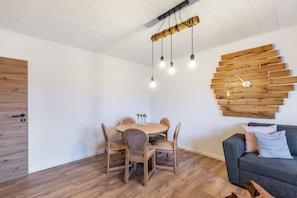 A dining area with a wooden table and chairs, a wall-mounted light fixture, and a grey sofa with pillows.