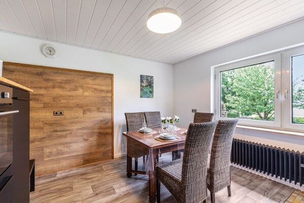 A dining area with a wooden table and wicker chairs, a window with a view of greenery, and a white ceiling with wooden beams. - Holiday Home 'Liebe' with Shared Garden, Balcony and Wi-Fi (Seesbach)