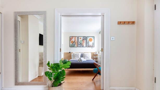 A bedroom with a bed, a large mirror, a potted plant, and artwork on the wall. - Classic 1BR - Notting Hill Gem (London)