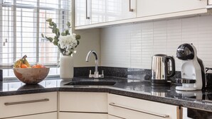 A kitchen with white cabinets, a black countertop, a stainless steel kettle, and a bowl of fruit. - Classic 1BR - Notting Hill Gem (London)