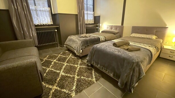 Ein Hotelzimmer mit zwei Betten, einem Sofa, einem gemusterten Teppich und einem Fenster mit Vorhängen.