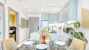 A modern dining area with a glass table, beige upholstered chairs, and a vase of flowers. - PVH - Exquisite 1BR - Binghatti Canal (Dubai)