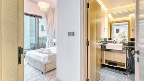 A modern hotel room with a large bed, a bathroom with a vanity and sink, and a view of the outdoors. - PVH - Exquisite 1BR - Binghatti Canal (Dubai)