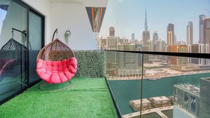 A balcony with a hanging chair, a green artificial turf floor, and a city view. - PVH - Exquisite 1BR - Binghatti Canal (Dubai)