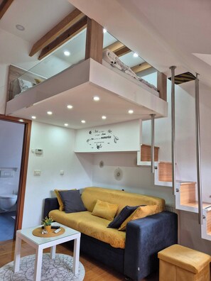 Un salon moderne avec un canapé, une table basse et un espace en mezzanine comprenant un meuble à chaussures.