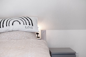 A bed with a patterned bedspread and a pillow with a black design and the word 'LOVE'.