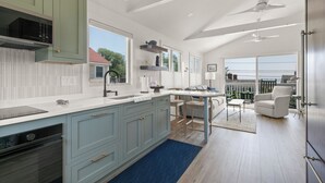 Eine moderne Küche mit hellblauen Schränken, einer weißen Arbeitsplatte und einem eingebauten Backofen. Es gibt einen Essbereich mit Tisch und Stühlen sowie einen Blick ins Freie durch große Fenster.