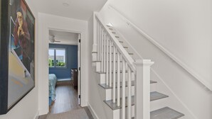 Eine Treppe mit weißen Geländern und Holzboden, die zu einem Schlafzimmer mit blauer Wand und Fenster hinaufführt.