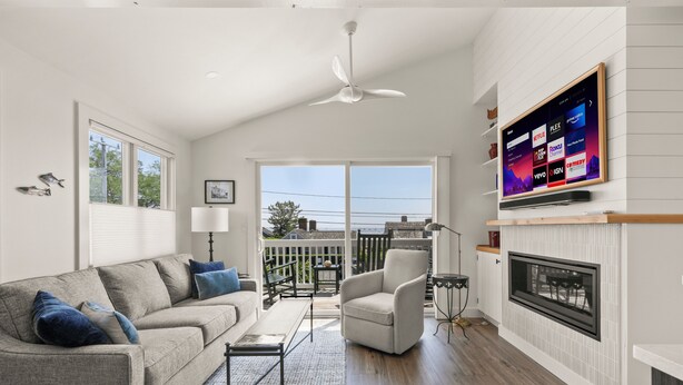 Ein modernes Wohnzimmer mit Sofa, Sessel und Kamin. Ein Flachbildfernseher ist an der Wand montiert, und es gibt einen Balkon mit Blick.