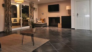 Una sala de estar moderna con chimenea, televisor de pantalla plana montado en la pared y un ventanal con cortinas.