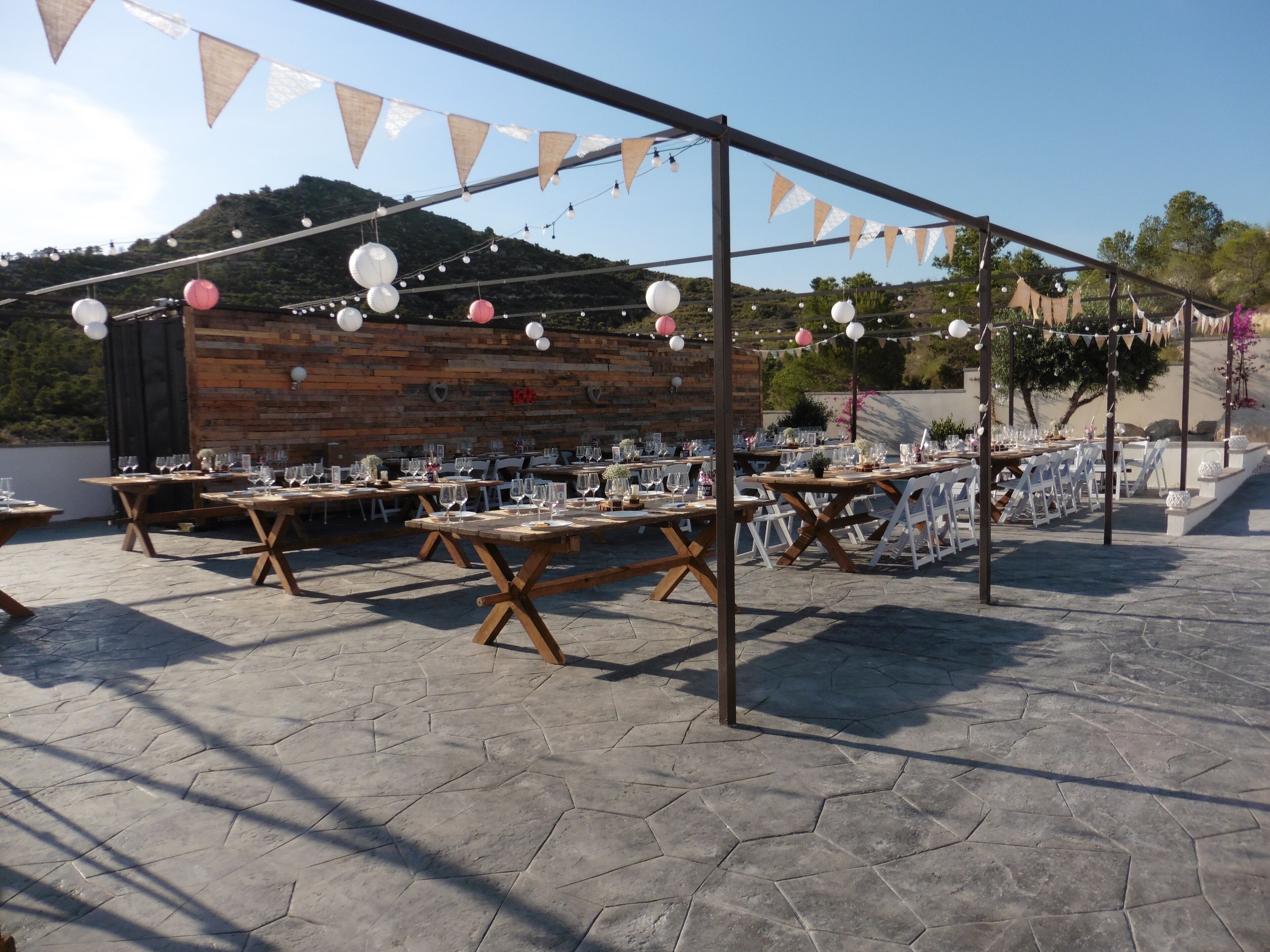 An outdoor dining area with hexagonal stone flooring, wooden tables, and white chairs.