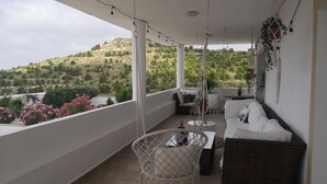Un balcón con una silla colgante, un sofá y una mesita. Hay plantas y una vista de un paisaje montañoso.