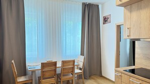 A kitchen with wooden cabinets, a dining table with chairs, and a window with curtains. - Riverside Apartment 9 (Hlavní město Praha)