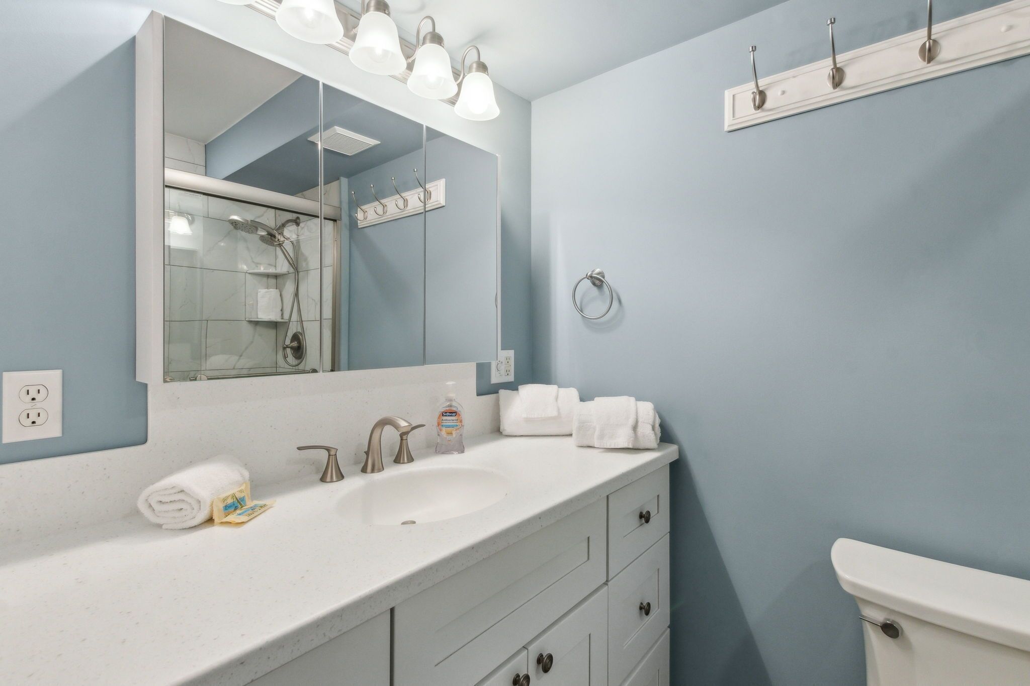 Une salle de bain avec un lavabo blanc, un grand miroir, un porte-serviettes et des toilettes.