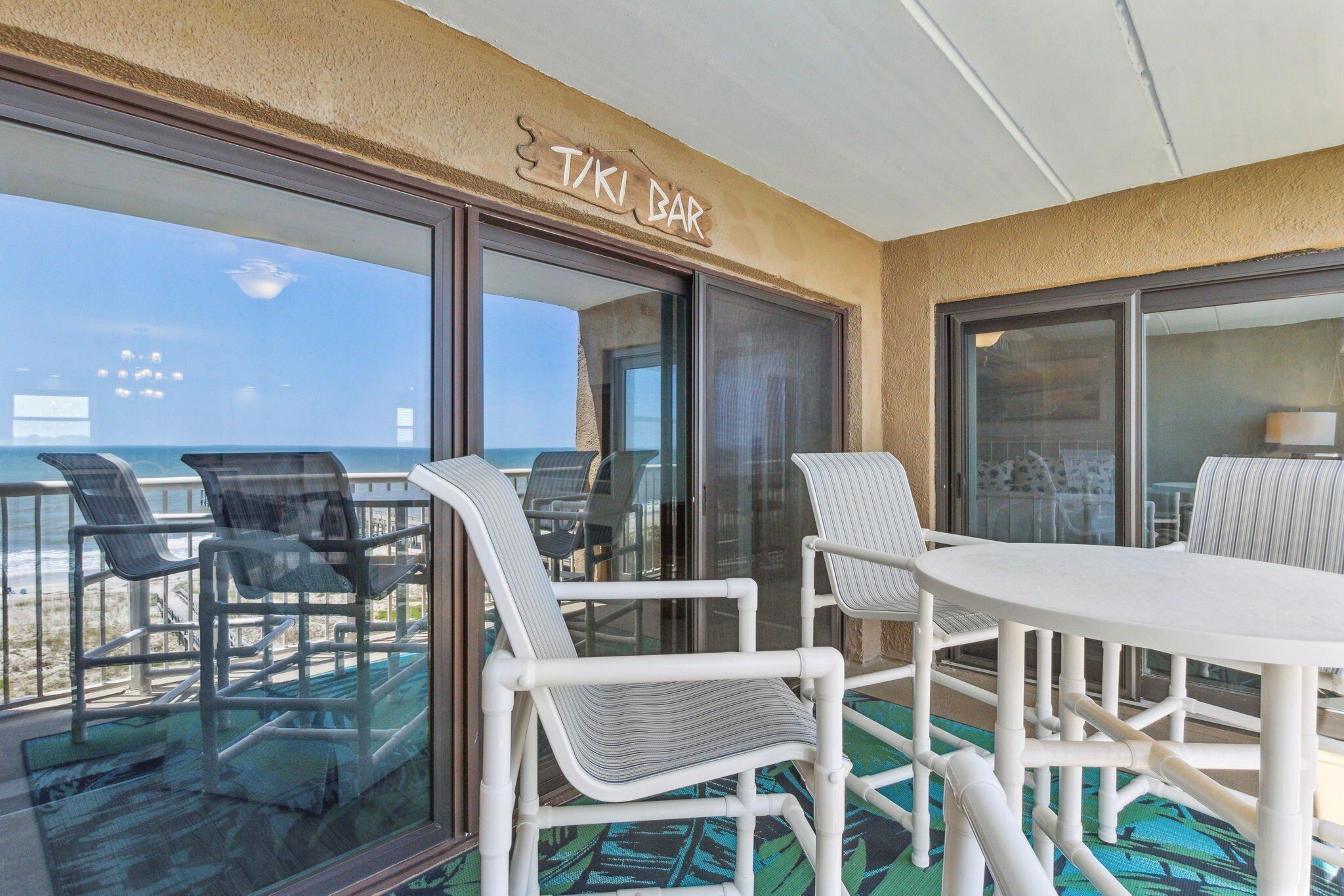 A TIKI bar area with a glass-enclosed balcony, white wicker furniture, and a view of the ocean.