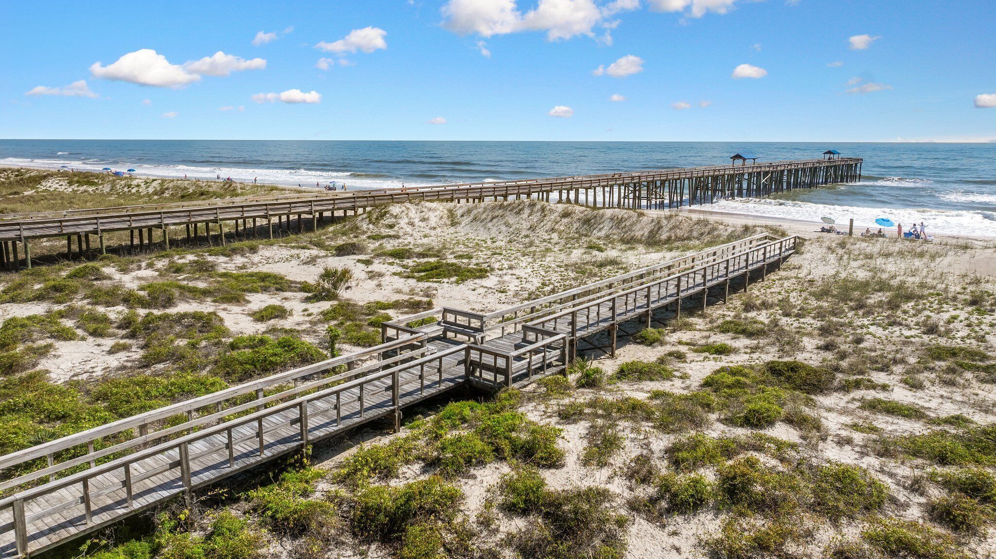 A beach with wooden walkways and a pier extending into the ocean.