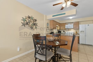 A dining area with a wooden table and chairs, a ceiling fan, and a kitchen in the background. - Spacious 3-Bedroom Condo in Wooded Fernandina Beach, Perfect for Family Getaways! (Fernandina Beach)