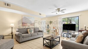 Ein Wohnzimmer mit grauem Sofa, einem Couchtisch, einem Fernseher und einem Deckenventilator.