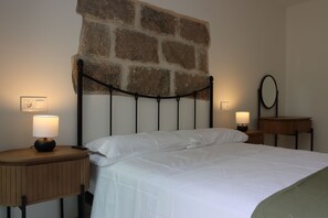 A neatly made bed with white linens, a stone accent wall, and bedside lamps. - La Tajuela Casa Rural (Bohonal de Ibor)