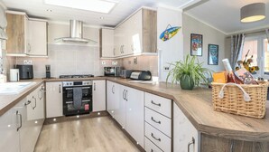A modern kitchen with a built-in oven, microwave, and toaster. There is a wooden countertop and a wicker basket with items on it. - Life's a Beach (Norwich)