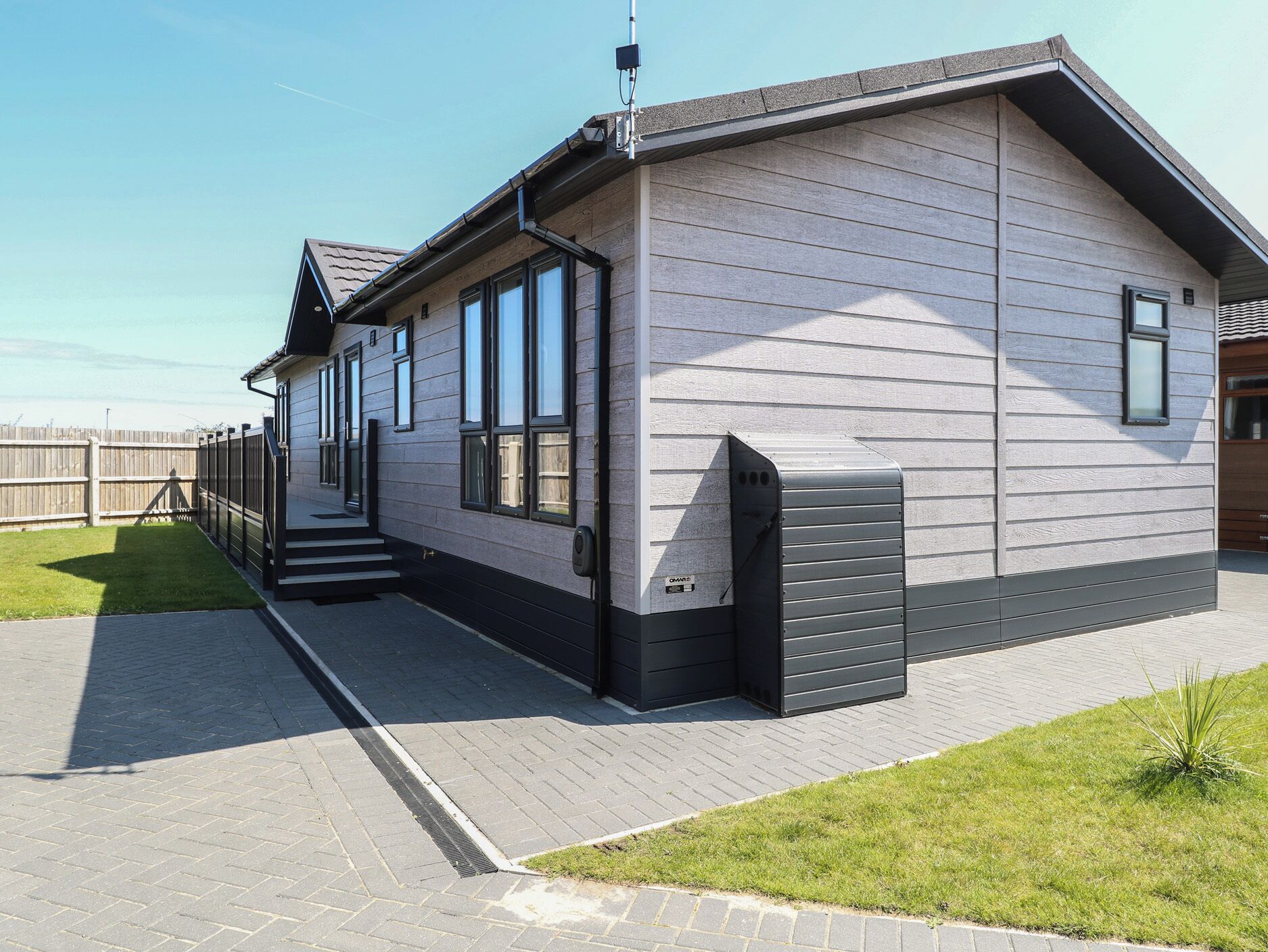 Una casa moderna a un piano con rivestimento esterno grigio, ampie finestre e un portone garage nero.