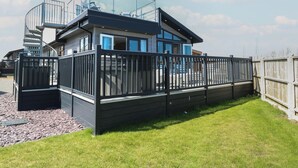 A modern two-story house with a glass balcony, a fenced yard, and a wooden deck. - Life's a Beach (Norwich)