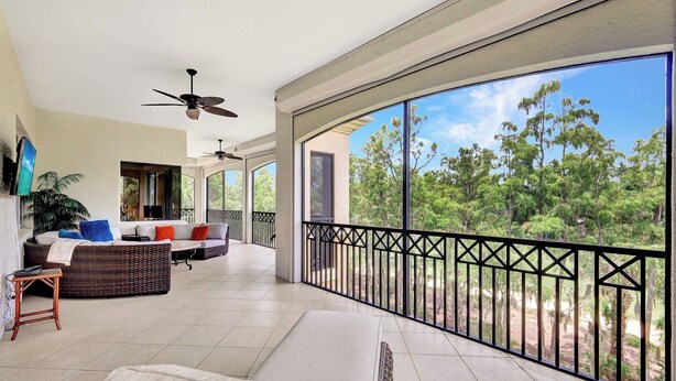 A spacious balcony with a view of trees, a wicker sofa, and a ceiling fan. - Castillo in Tiburon - Luxury Penthouse (Naples)