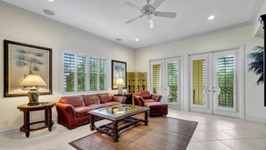A spacious living room with a brown leather sofa, a glass coffee table, and a ceiling fan. - Castillo in Tiburon - Luxury Penthouse (Naples)