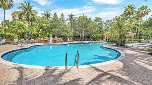A circular pool with a clear blue water, surrounded by lounge chairs and palm trees. - Castillo in Tiburon - Luxury Penthouse (Naples)