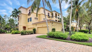 A two-story building with a yellow facade, numbered 103, featuring a brick driveway, palm trees, and well-maintained landscaping. - Castillo in Tiburon - Luxury Penthouse (Naples)