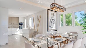 A modern dining area with a glass table, white chairs, and a contemporary pendant light.