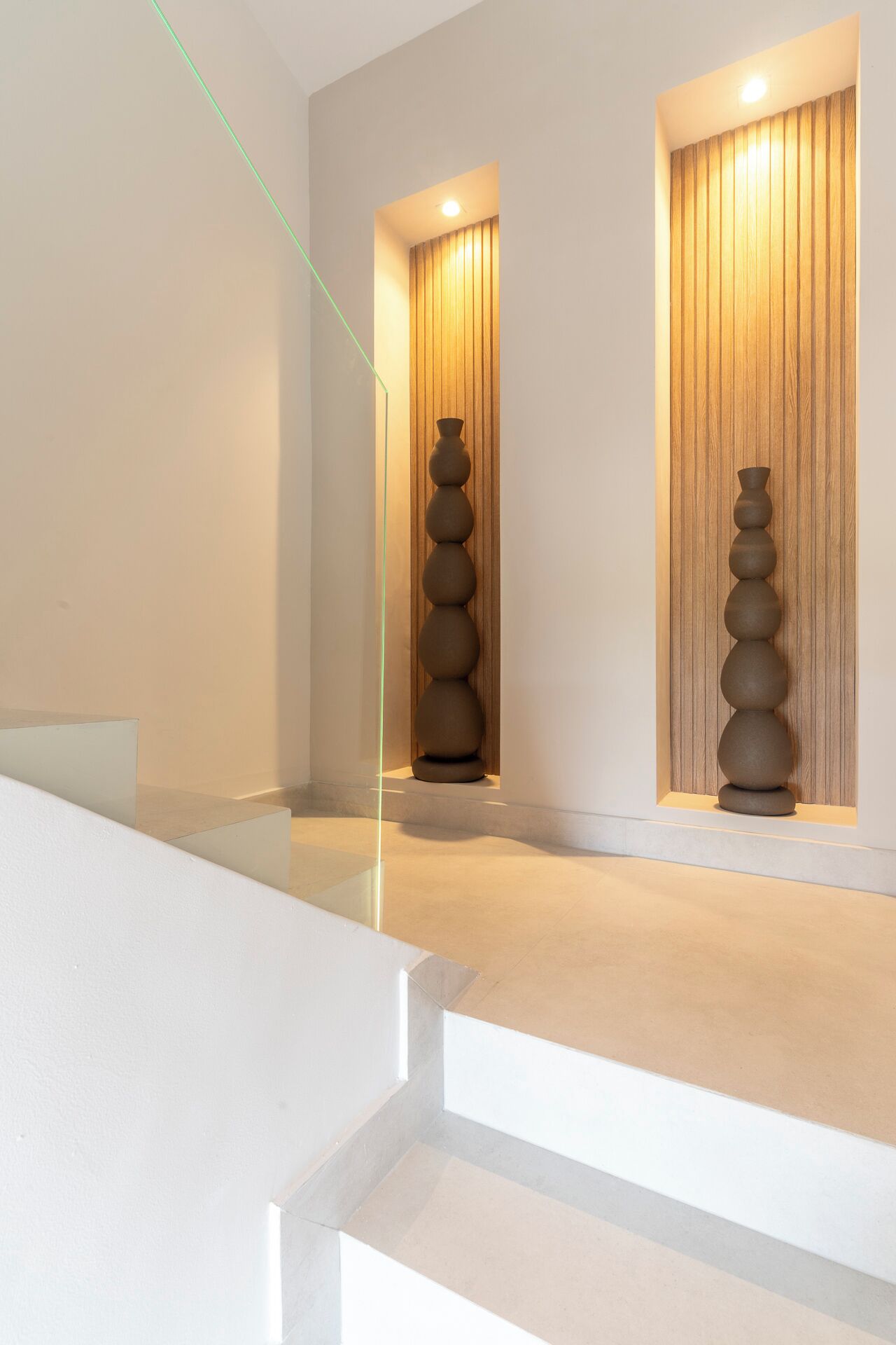 Een modern interieur met een minimalistisch ontwerp, met een centrale trap, twee houten wandpanelen met ingebouwde verlichting, en een reeks bolvormige sculpturen.