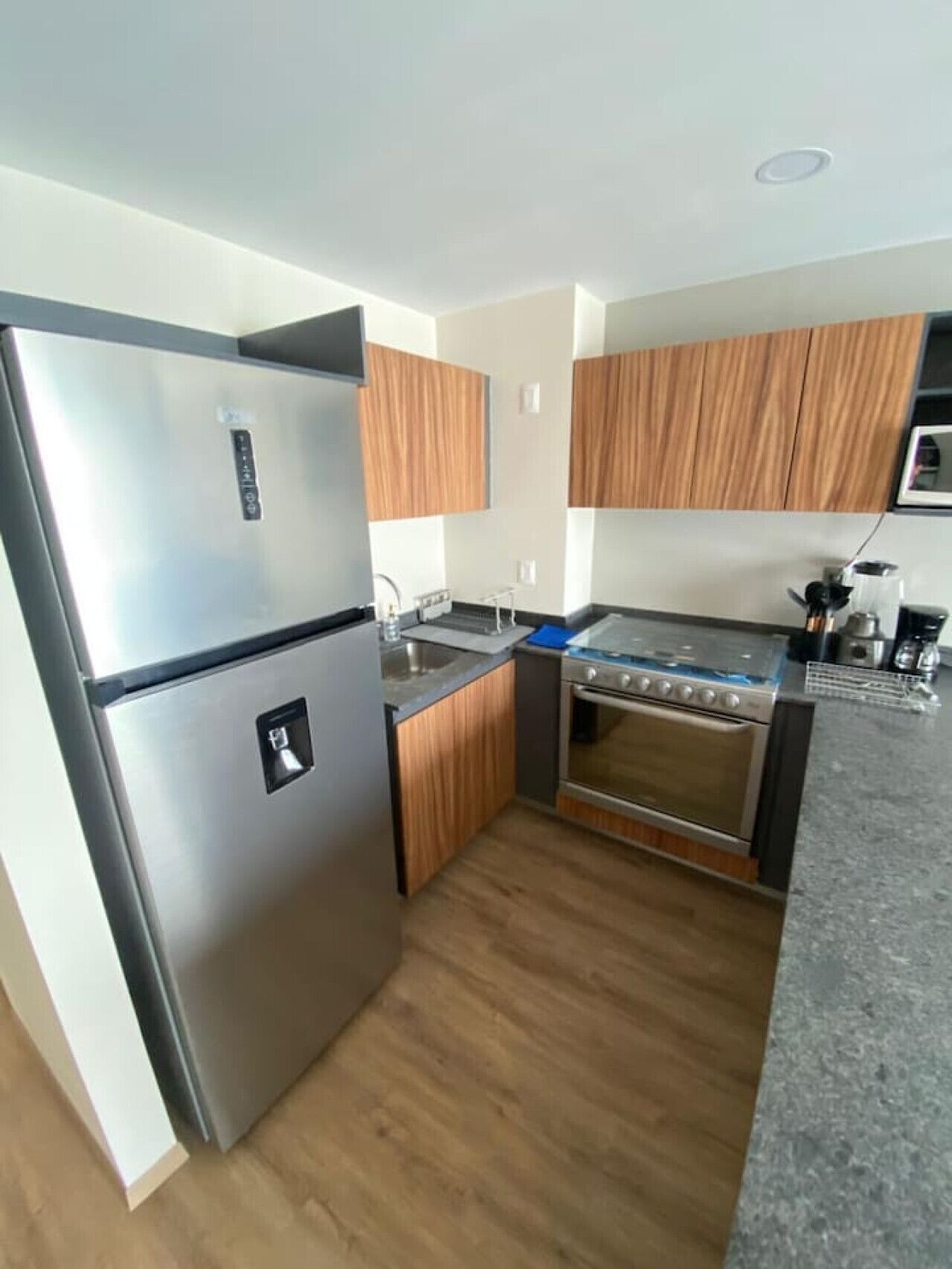 A compact kitchen with a stainless steel refrigerator, a built-in oven, and wooden cabinets.