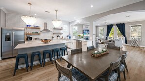 A modern kitchen with a central island, bar stools, and a dining table with chairs. - Tropical Paradise: 4BR Island Home w/ Pool & Bay Views (Anna Maria)
