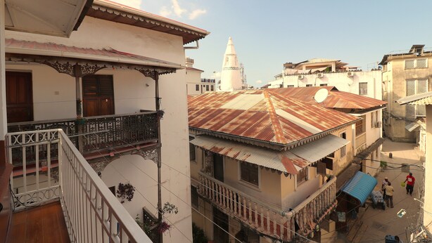 A multi-story building with balconies, a satellite dish, and a traditional tower in the background. - 2BR in Stone Town – Near Ferry Terminal, Museums & Cultural Sights (Stone Town)