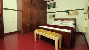 A bedroom with a wooden wardrobe, a bed with a red bedspread, a wooden bench, and a ceiling fan. - 2BR in Stone Town – Near Ferry Terminal, Museums & Cultural Sights (Stone Town)