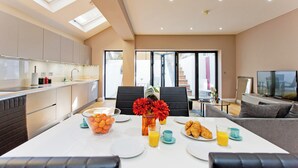 A modern kitchen with a dining area, a sofa, and a TV. - Prime Central Base! 3BR/3BA Apt w/ Courtyard. Ideal for Families and Groups. (London)