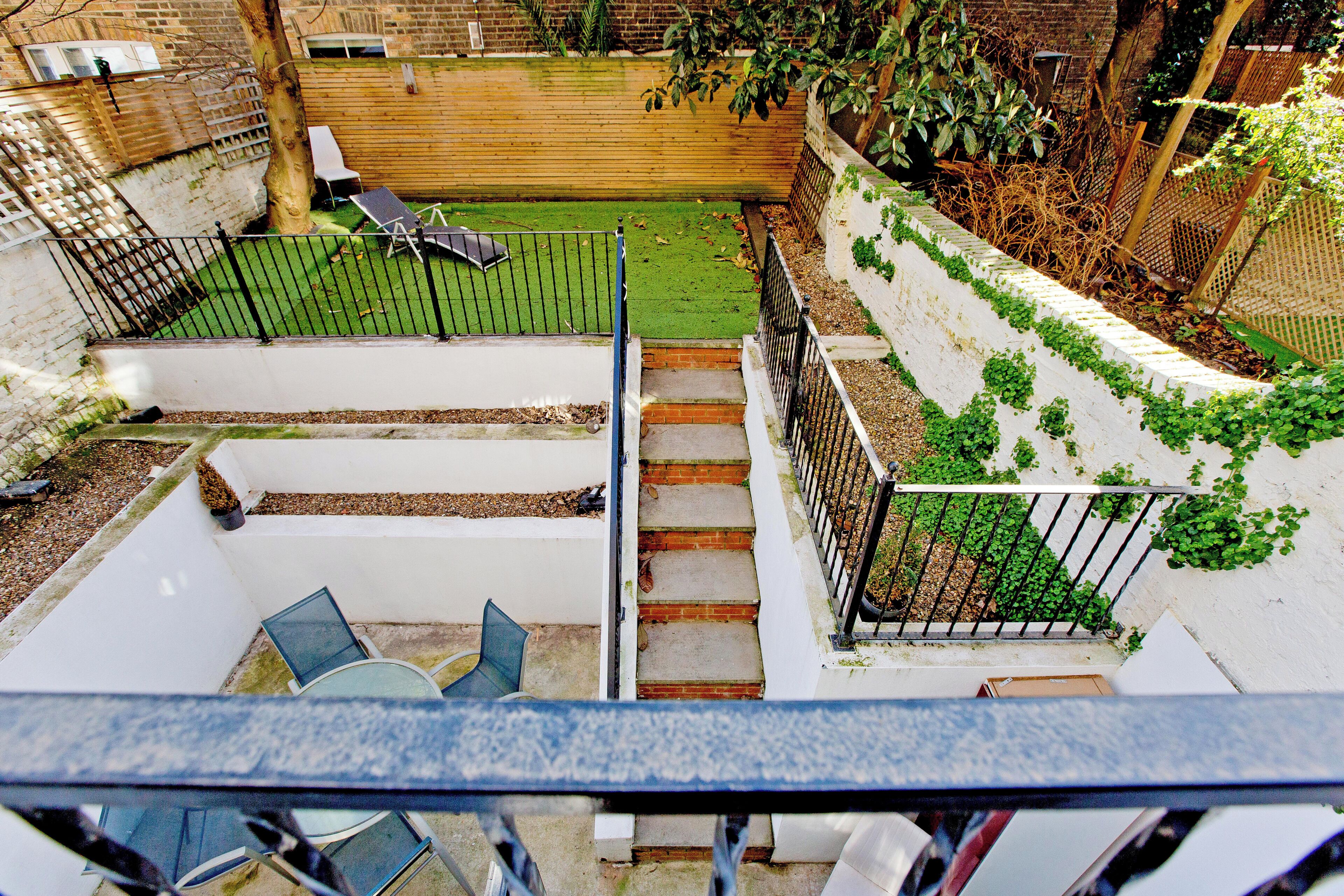 Une vue depuis un balcon donnant sur une cour arrière avec une pelouse verdoyante, une clôture en bois et un escalier menant au niveau inférieur.